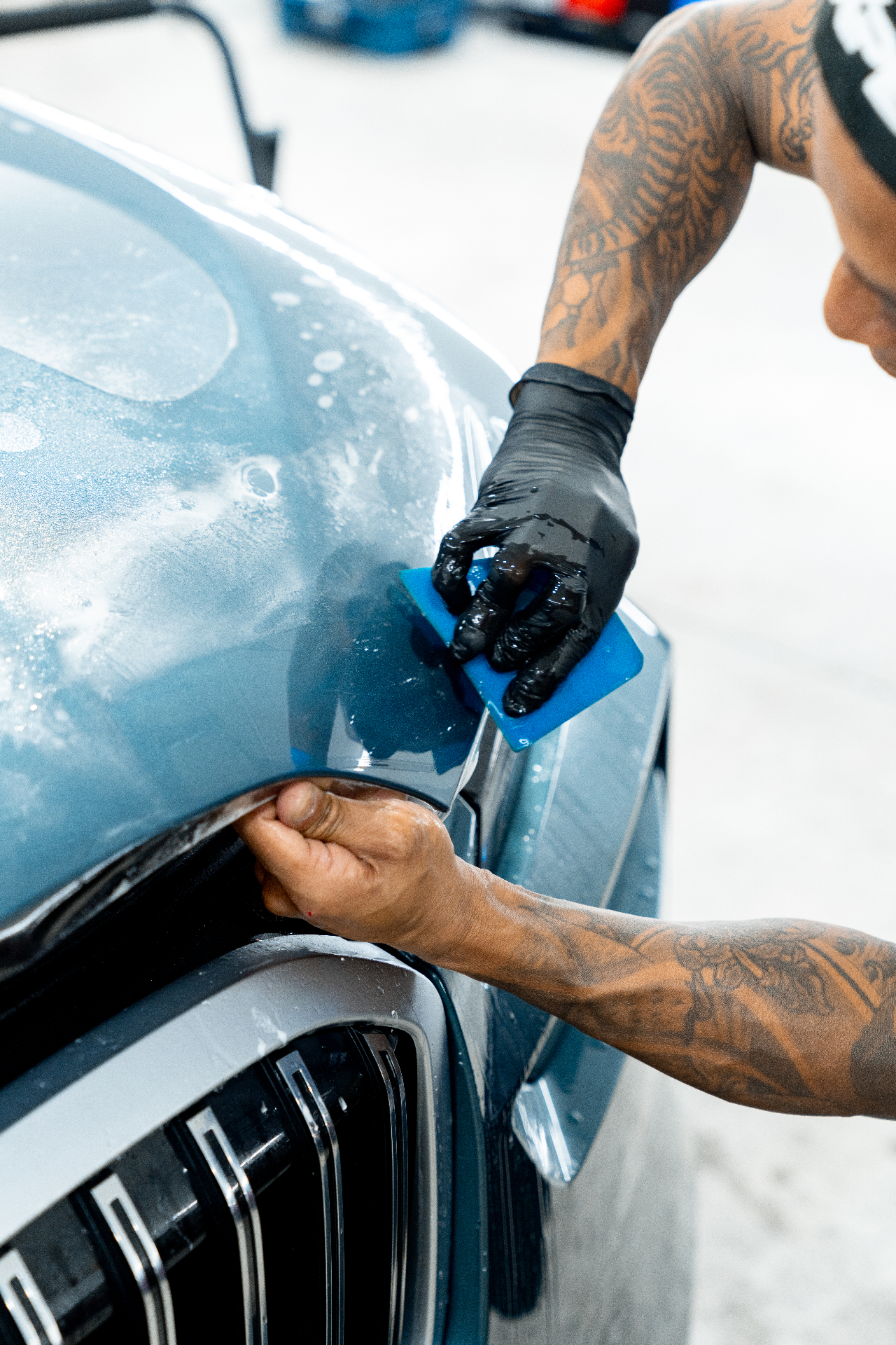 XPEL certified installer squeegeeing paint protection film on a deep blue sports car door