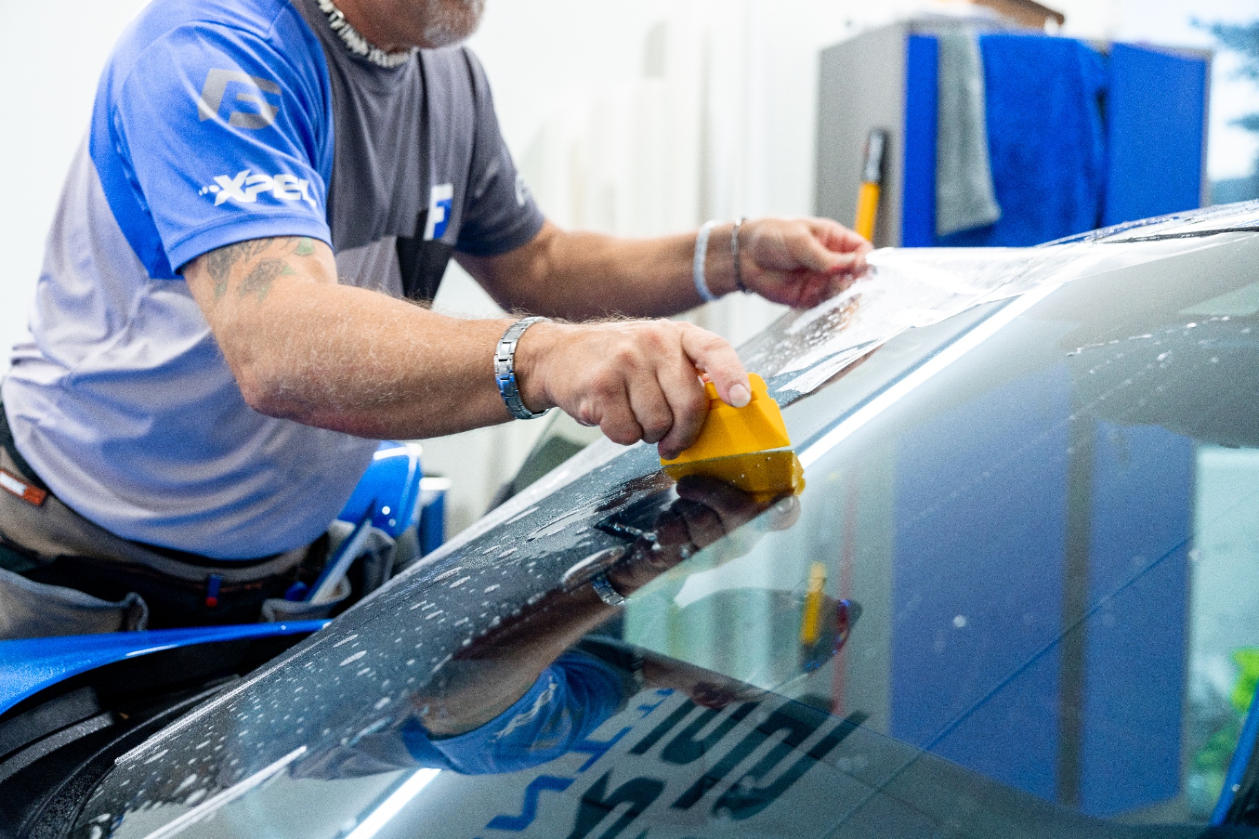 XPEL installer squeegeeing windshield protection film onto a vehicle windshield