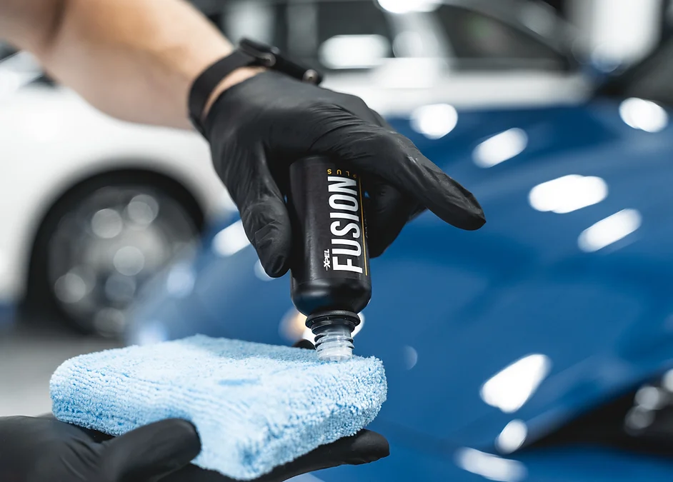 Gloved technician applying XPEL ceramic coating with an applicator pad on a deep blue hood