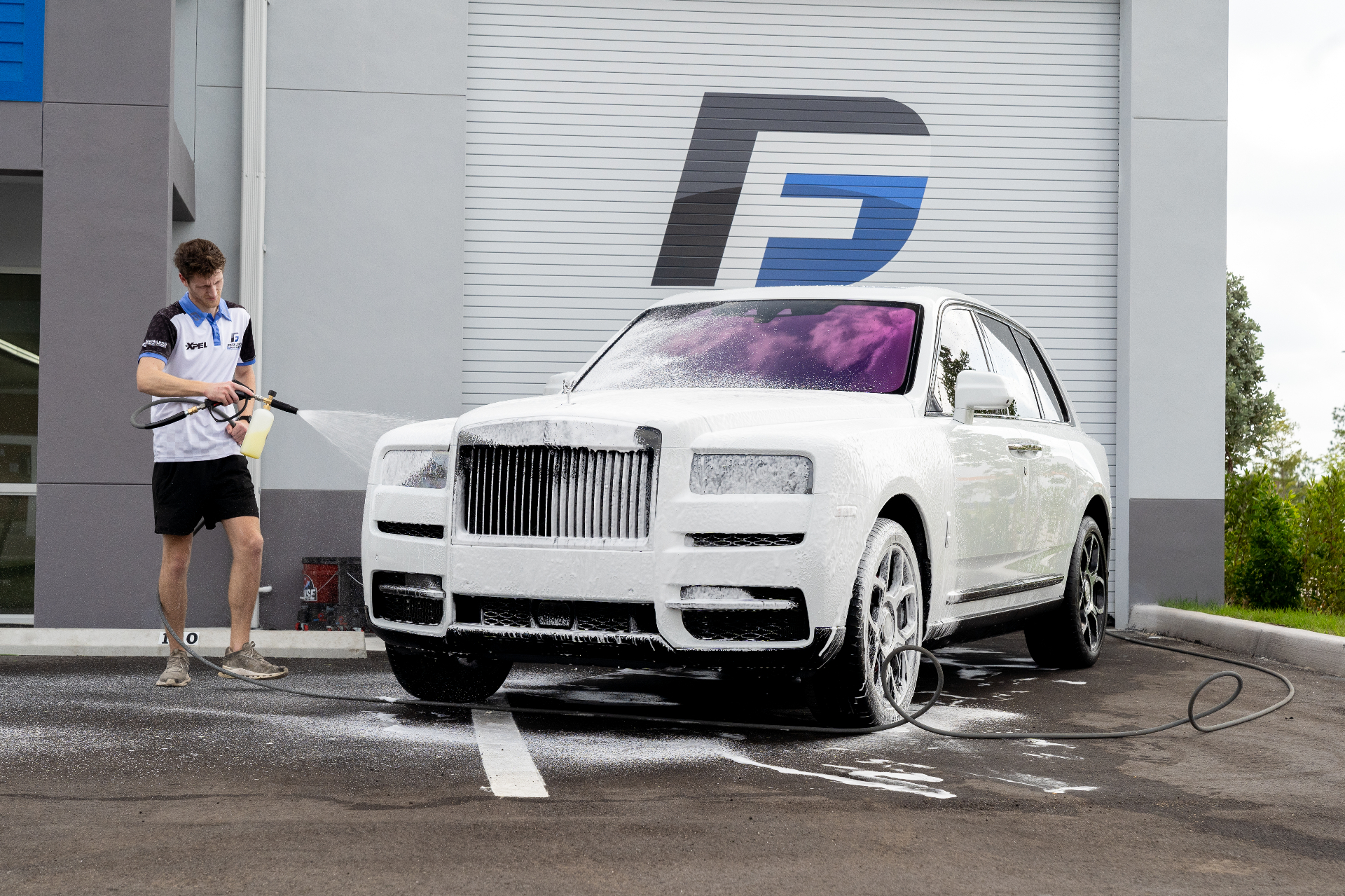 Detailer foam-cannon washing a white Rolls-Royce Cullinan in front of the Fort Myers shop